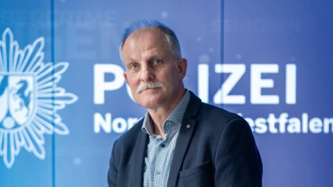 Chief Superintendent Ralf Trippe can be seen in the new concept store in Cologne. He is standing in front of a screen showing the NRW police logo and the words "Polizei Nordrhein-Westfahlen" in white lettering on a blue background. There are several tablets on tables in front of him.